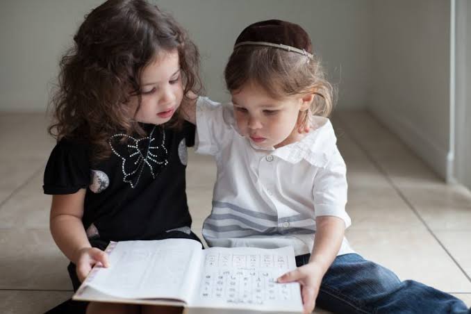 Two young girls sitting together, reading from an open book